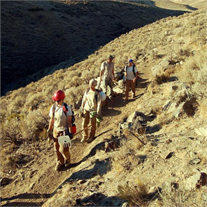 Youth hiking in a line along a dry, rugged hillside trail.