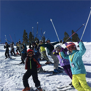 Children posing with skis on a snowy mountain slope.