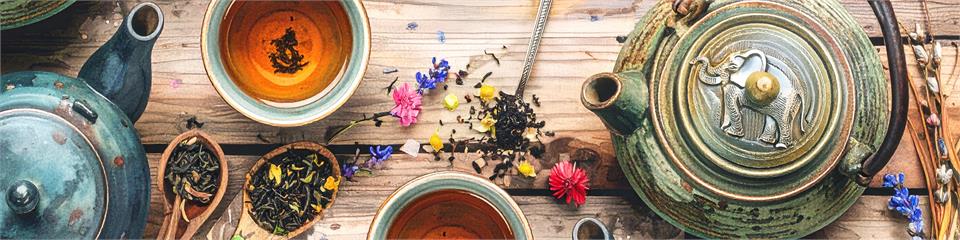 Tea-making setup with teapots, tea leaves, and flowers on a wooden surface