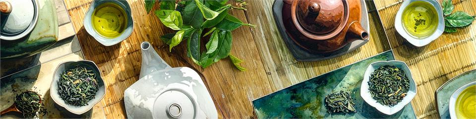 Tea-making setup with teapot, tea leaves, and cups on a wooden surface.