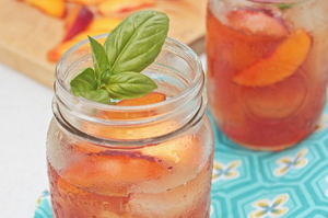 Iced tea with peach slices and basil garnish in mason jars.